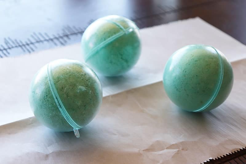 teal bath bombs with hidden toys in their mold on a piece of parchment paper