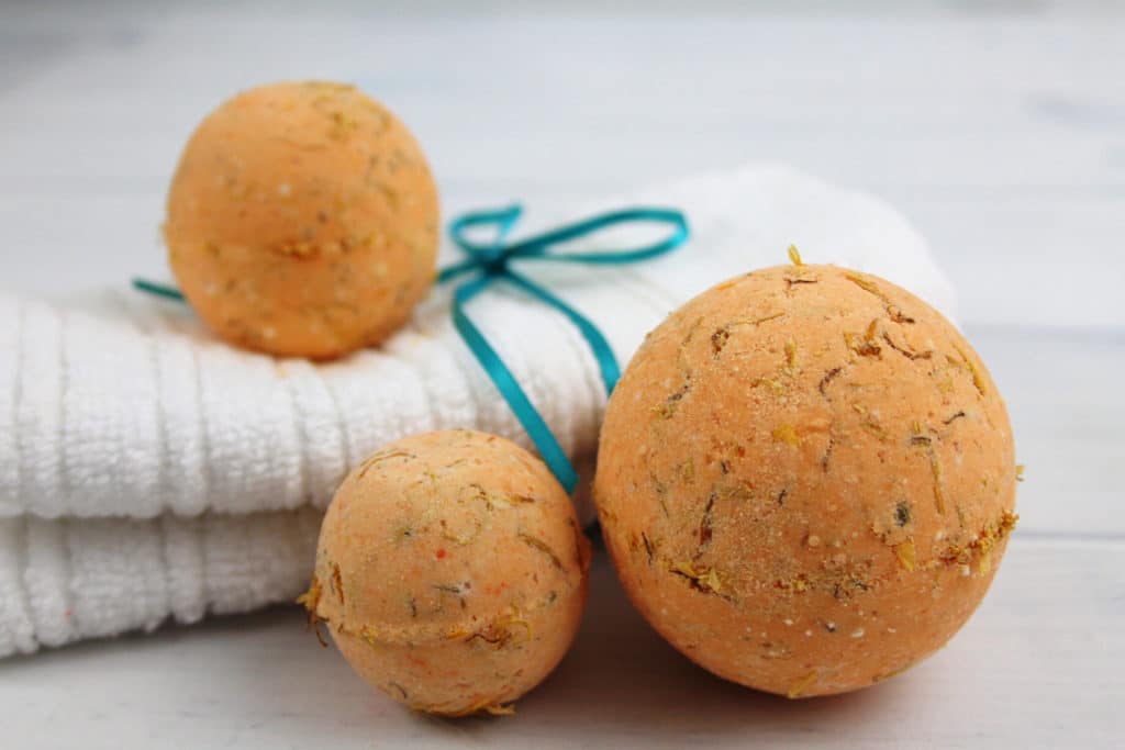 Three homemade calendula bath bombs on a white towel with a turquoise string